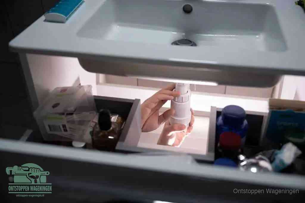 Een pompfles met zeep boven een wastafel, de heet water en afwasmiddel-methode om een vetprop in de afvoer los te maken in Wageningen