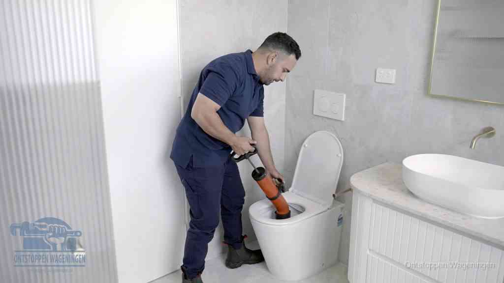 Een monteur buigt over een wandcloset en duwt met de hand een persluchtontstopper in de toiletpot om de verstopping handmatig los te maken in Wageningen