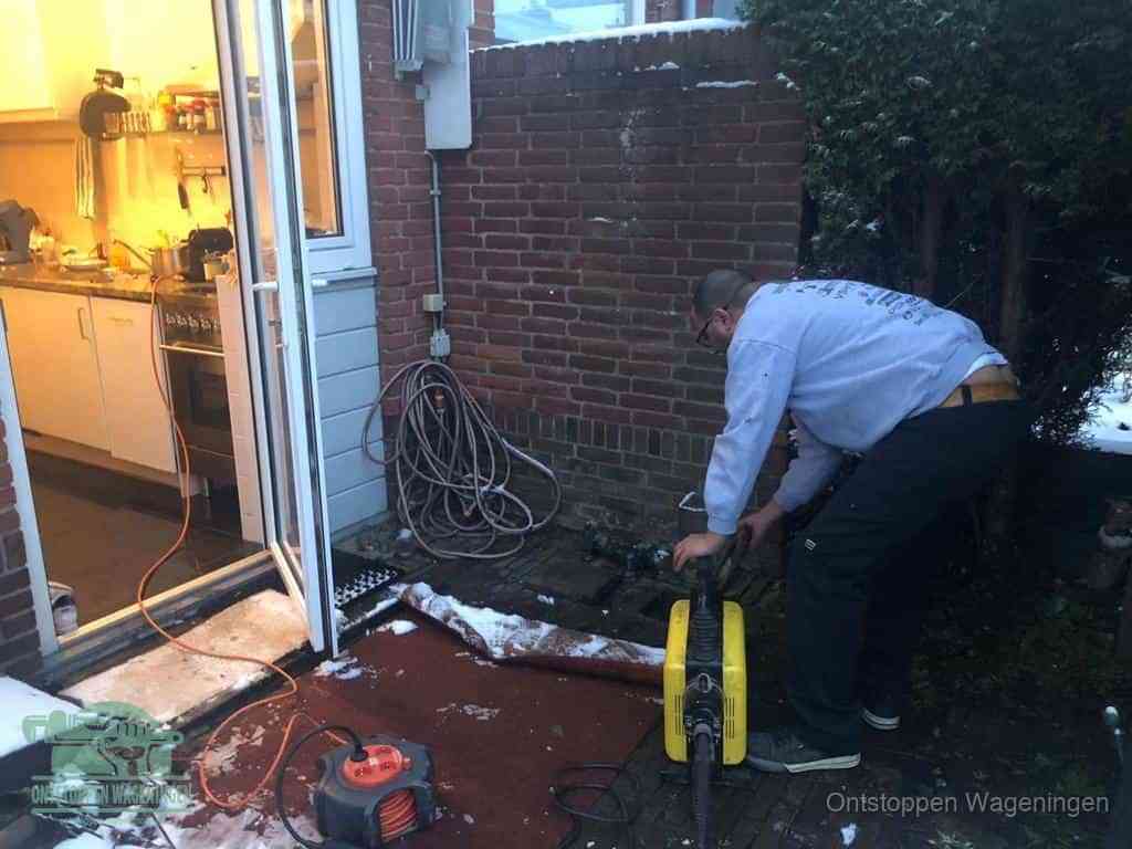 Een monteur werkt buiten bij een open riool-/grondput met een elektrische ontstoppingsmachine om een verborgen afvoerprobleem op te sporen in Wageningen