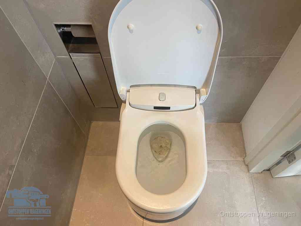 Een wit hangtoilet waarin een prop wc-papier op het water blijft drijven, een duidelijk signaal van een verstopte wc in Wageningen