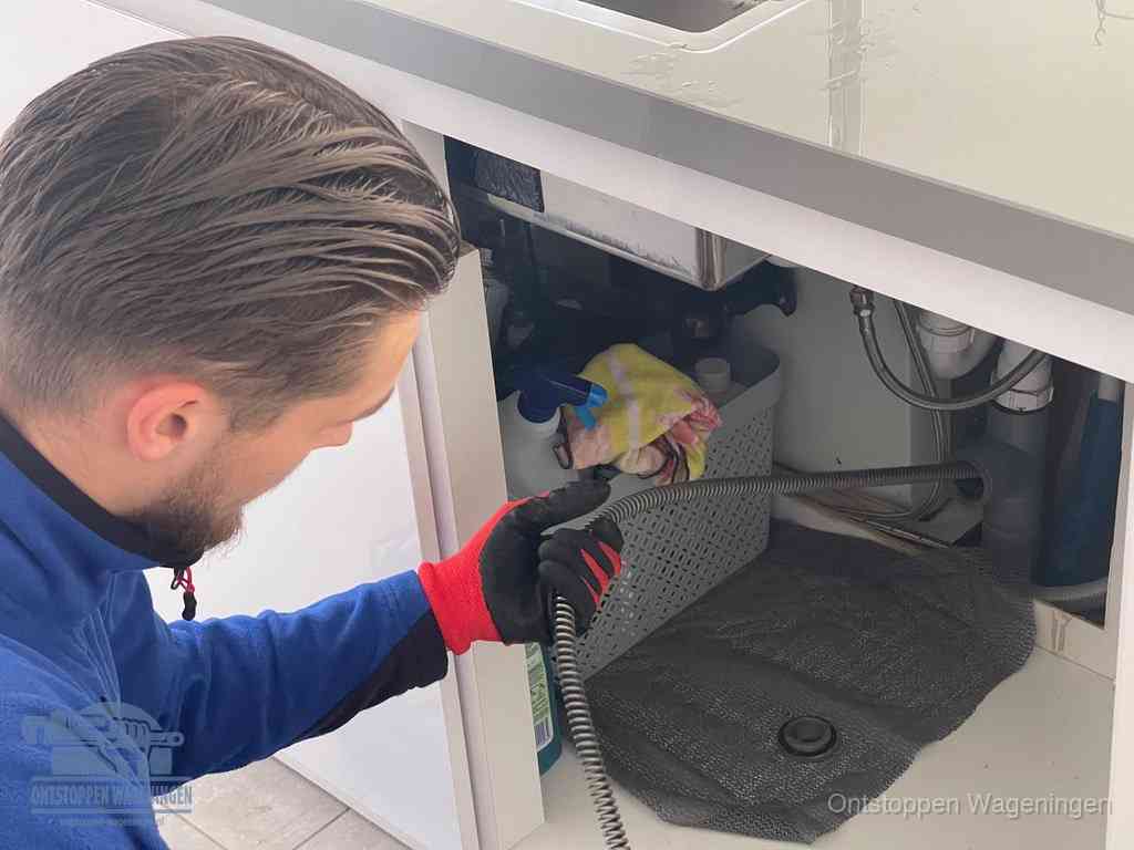 Een monteur voert een flexibele ontstoppingsveer in de afvoer om een verstopping voorbij de bocht van het toilet te bereiken in Wageningen