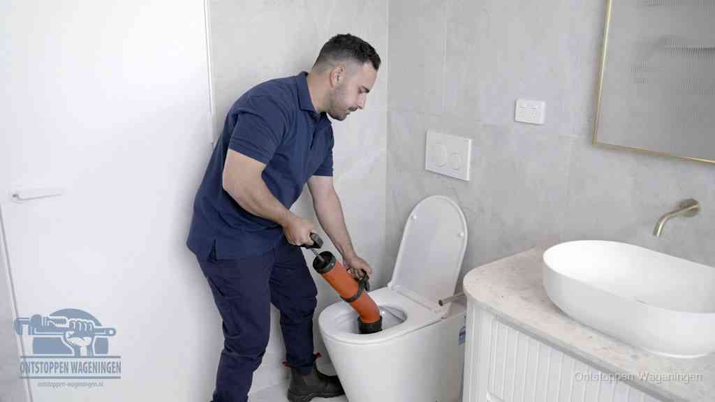 Een monteur gebruikt een handmatige perspomp (toiletontstopper) op een wandcloset tijdens het professioneel wc ontstoppen in Wageningen