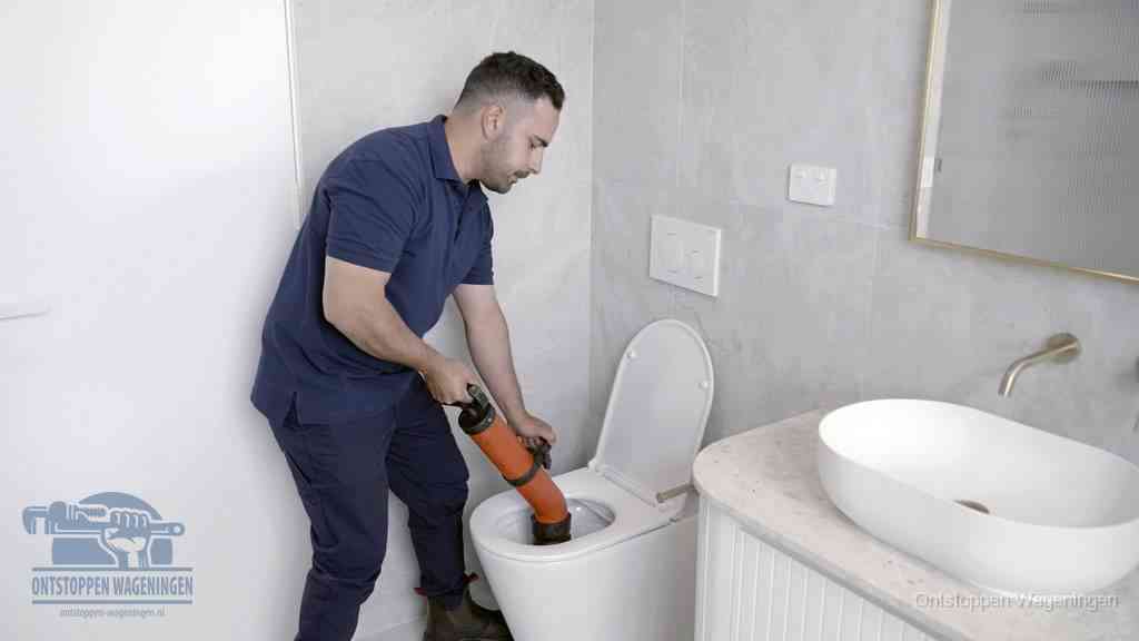 Een man gebruikt een handmatige luchtdruk-ontstopper in een modern betegeld toilet om zelf de wc te ontstoppen in Wageningen